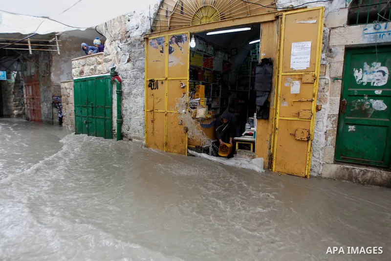 A Palestinian man cleans up flooded water outside his shop following heavy rains in the West Bank city of Hebron, on March 28, 2016. Photo by Wisam Hashlamoun