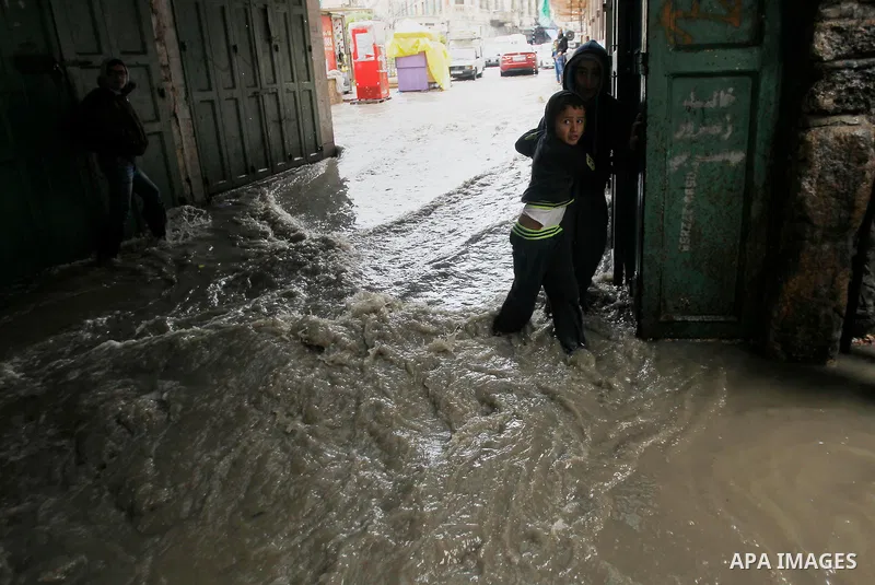 Palestinians walk in a street flooded by rain water in the West Bank city of Hebron, on March 28, 2016. Photo by Wisam Hashlamoun