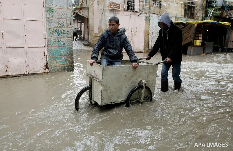 Palestinians walk in a street flooded by rain water in the West Bank city of Hebron, on March 28, 2016. Photo by Wisam Hashlamoun