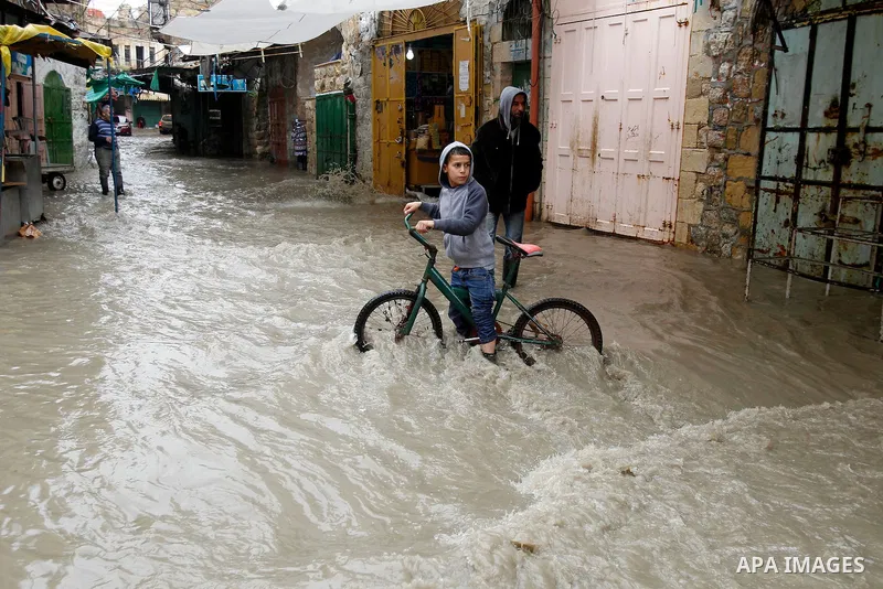 A Palestinian boy rides at a street flooded by rain water in the West Bank city of Hebron, on March 28, 2016. Photo by Wisam Hashlamoun