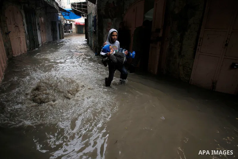 Palestinians walk in a street flooded by rain water in the West Bank city of Hebron, on March 28, 2016. Photo by Wisam Hashlamoun