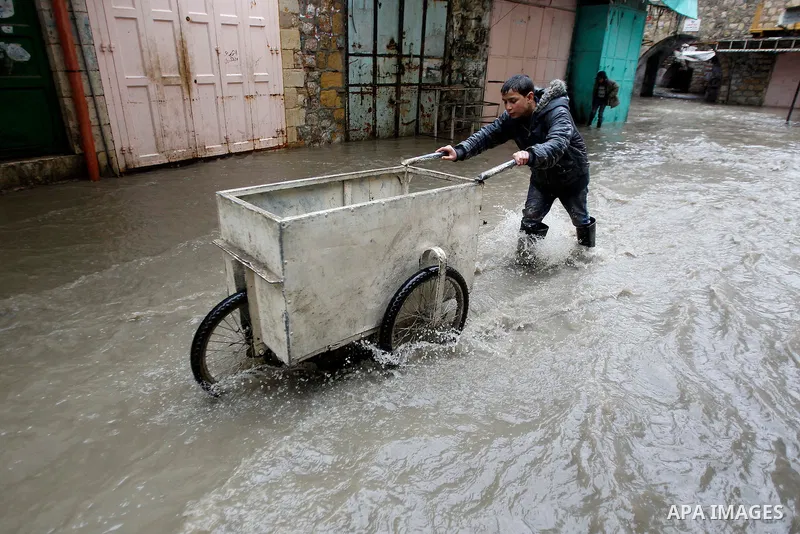 Palestinians walk in a street flooded by rain water in the West Bank city of Hebron, on March 28, 2016. Photo by Wisam Hashlamoun