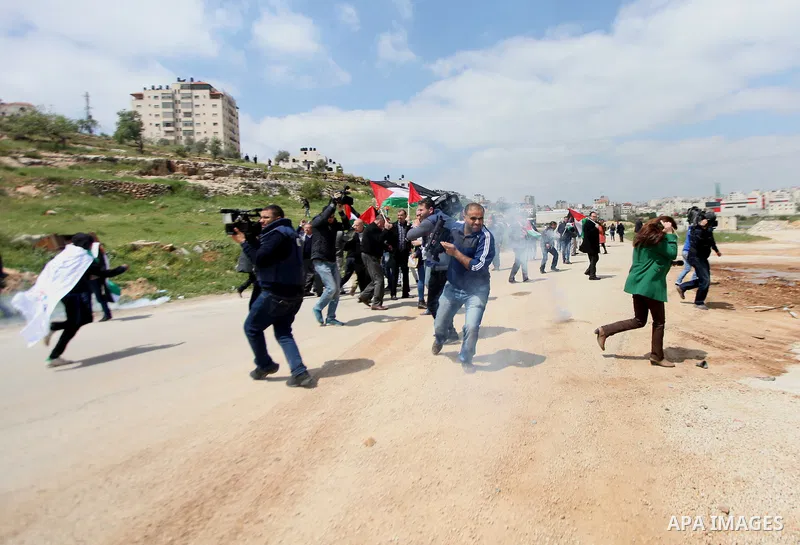 Palestinian journalists run for cover from tear gas fired by Israeli security forces during a demonstration to mark Land Day outside the compound of the Israeli-run Ofer prison near Betunia in the Israeli occupied West B...