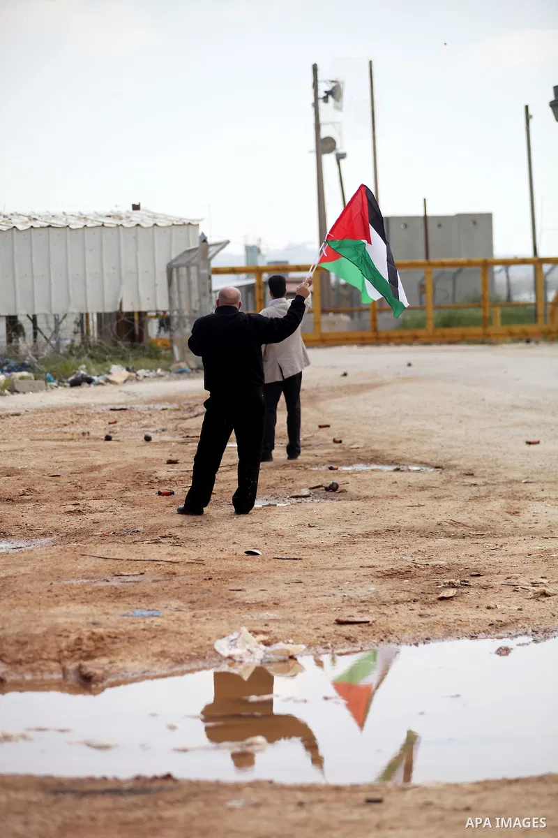 Palestinian protesters wave their national flag in front of Israeli security forces as they mark Land Day outside the compound of the Israeli-run Ofer prison near Betunia in the Israeli occupied West Bank on March 30, 20...