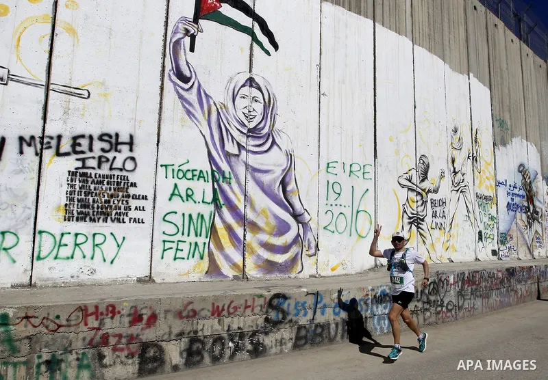 A participant runs past the controversial Israeli barrier during the annual Right to Movement Palestine Marathon in the West Bank town of Bethlehem April 1, 2016. Photo by Wisam Hashlamoun