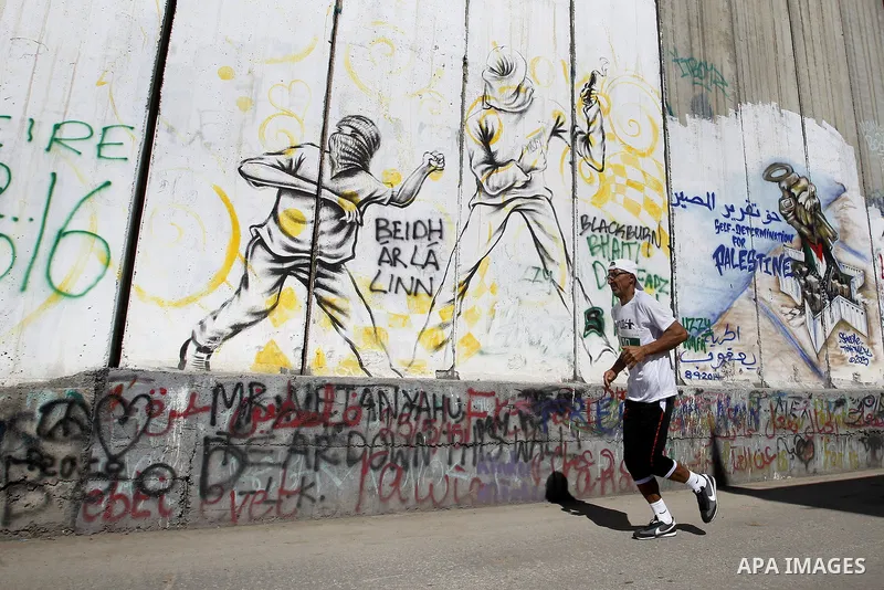 A participant runs past the controversial Israeli barrier during the annual Right to Movement Palestine Marathon in the West Bank town of Bethlehem April 1, 2016. Photo by Wisam Hashlamoun