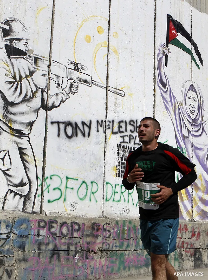 A participant runs past the controversial Israeli barrier during the annual Right to Movement Palestine Marathon in the West Bank town of Bethlehem April 1, 2016. Photo by Wisam Hashlamoun