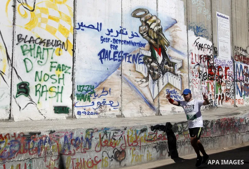 A participant runs past the controversial Israeli barrier during the annual Right to Movement Palestine Marathon in the West Bank town of Bethlehem April 1, 2016. Photo by Wisam Hashlamoun