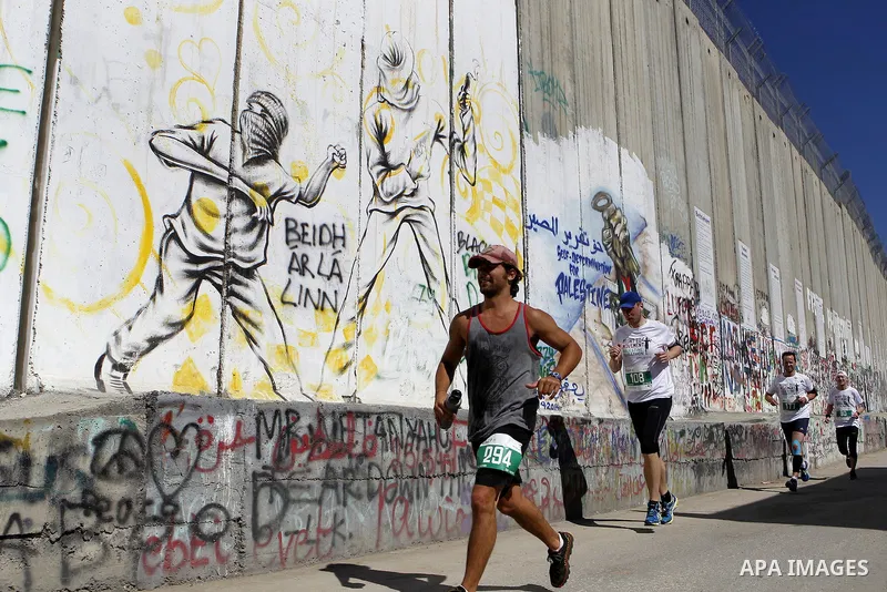 A participant runs past the controversial Israeli barrier during the annual Right to Movement Palestine Marathon in the West Bank town of Bethlehem April 1, 2016. Photo by Wisam Hashlamoun