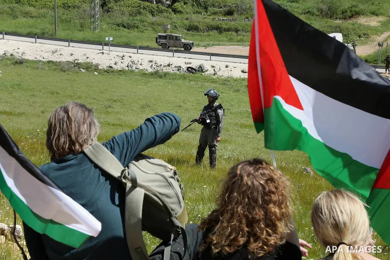 Palestinian protesters wave national flags in front of Israeli security forces during clashes following a march against Palestinian land confiscation on April 1, 2016 in the West Bank village of Nabi Saleh near Ramallah....