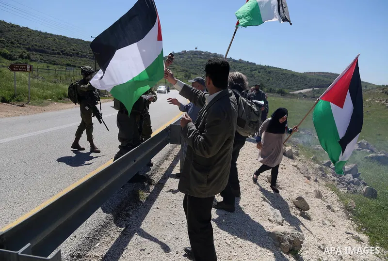 Palestinian protesters wave national flags in front of Israeli security forces during clashes following a march against Palestinian land confiscation on April 1, 2016 in the West Bank village of Nabi Saleh near Ramallah....