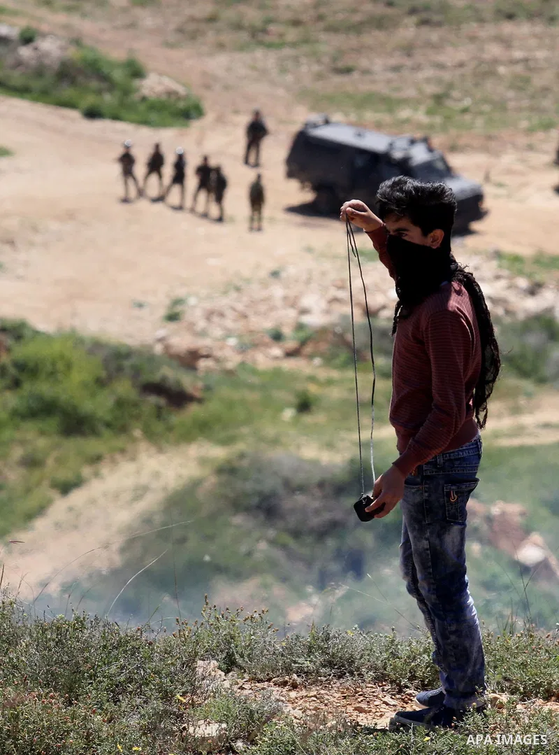 A Palestinian protester uses a slingshot to hurl stones toward Israeli security forces during clashes following a demonstration against Jewish settlements in the West Bank village of Qaryout near Nablus on April 01, 2016...