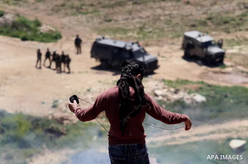 A Palestinian protester uses a slingshot to hurl stones toward Israeli security forces during clashes following a demonstration against Jewish settlements in the West Bank village of Qaryout near Nablus on April 01, 2016...