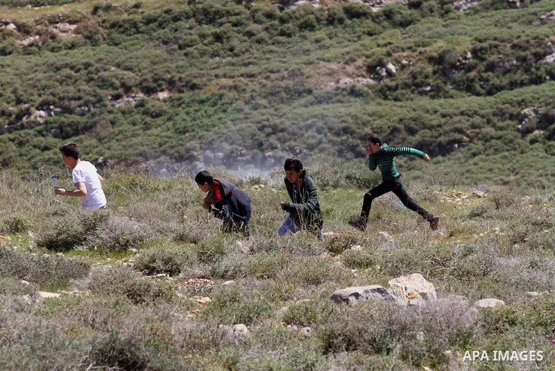 Palestinian protesters run for cover from tear gas fired by Israeli security forces during clashes following a demonstration against Jewish settlements in the West Bank village of Qaryout near Nablus on April 01, 2016. P...