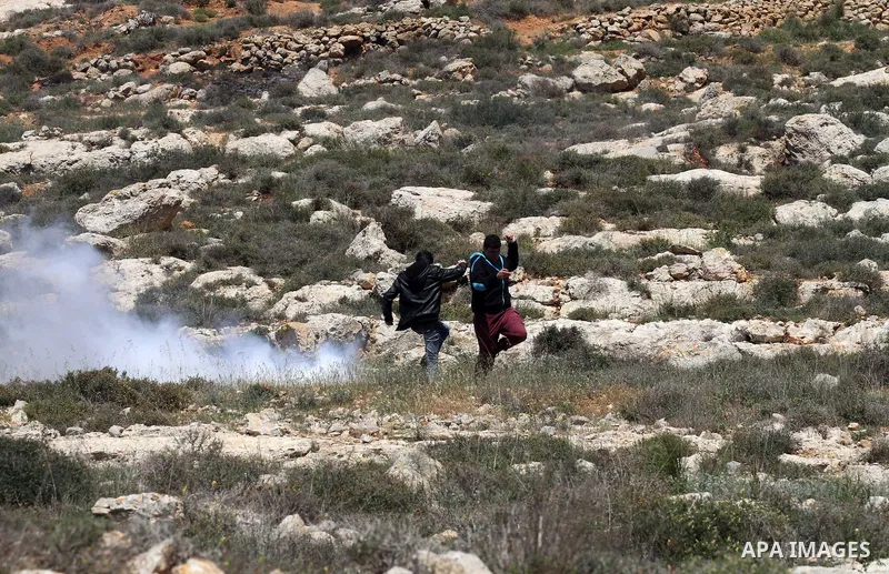 Palestinian protesters run for cover from tear gas fired by Israeli security forces during clashes following a demonstration against Jewish settlements in the West Bank village of Qaryout near Nablus on April 01, 2016. P...