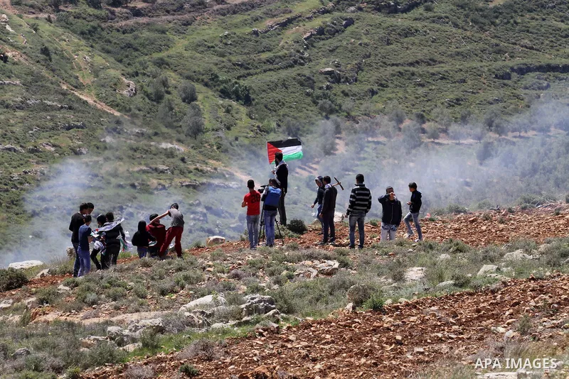 Palestinian protesters run for cover from tear gas fired by Israeli security forces during clashes following a demonstration against Jewish settlements in the West Bank village of Qaryout near Nablus on April 01, 2016. P...