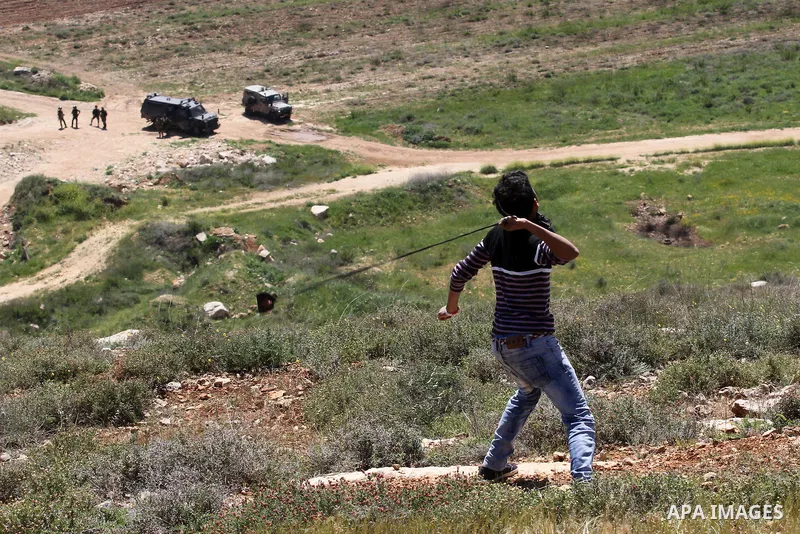 A Palestinian protester uses a slingshot to hurl stones toward Israeli security forces during clashes following a demonstration against Jewish settlements in the West Bank village of Qaryout near Nablus on April 01, 2016...
