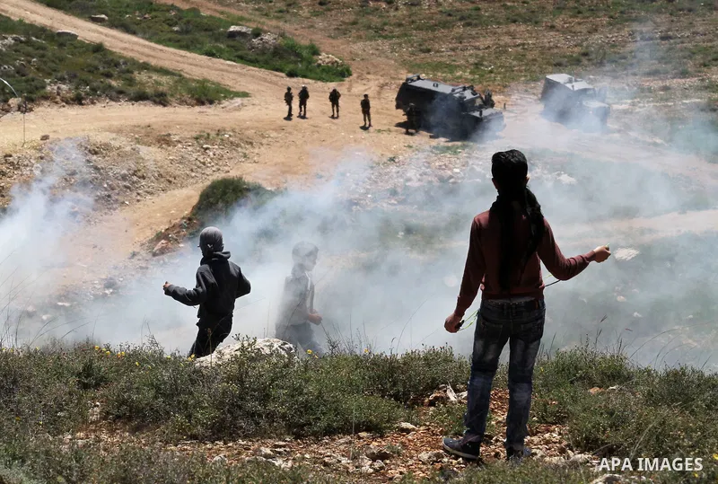 Palestinian protesters use a slingshot to hurl stones toward Israeli security forces during clashes following a demonstration against Jewish settlements in the West Bank village of Qaryout near Nablus on April 01, 2016....