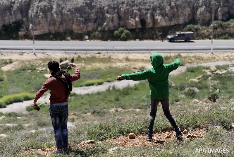 Palestinian protesters use a slingshot to hurl stones toward Israeli security forces during clashes following a demonstration against Jewish settlements in the West Bank village of Qaryout near Nablus on April 01, 2016....