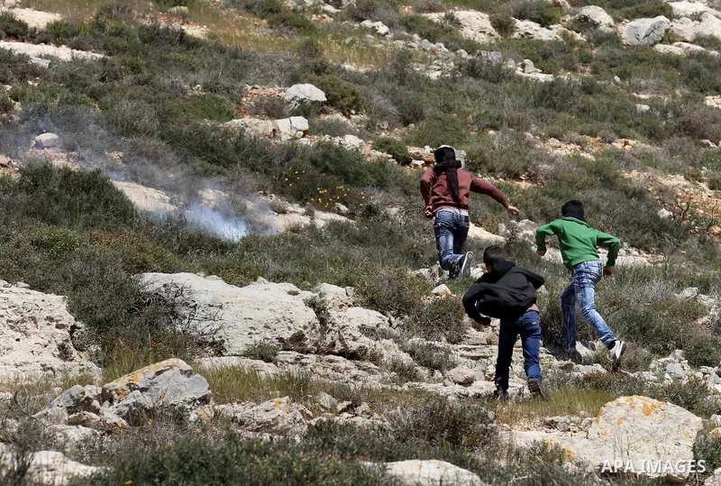 Palestinian protesters run for cover from tear gas fired by Israeli security forces during clashes following a demonstration against Jewish settlements in the West Bank village of Qaryout near Nablus on April 01, 2016. P...