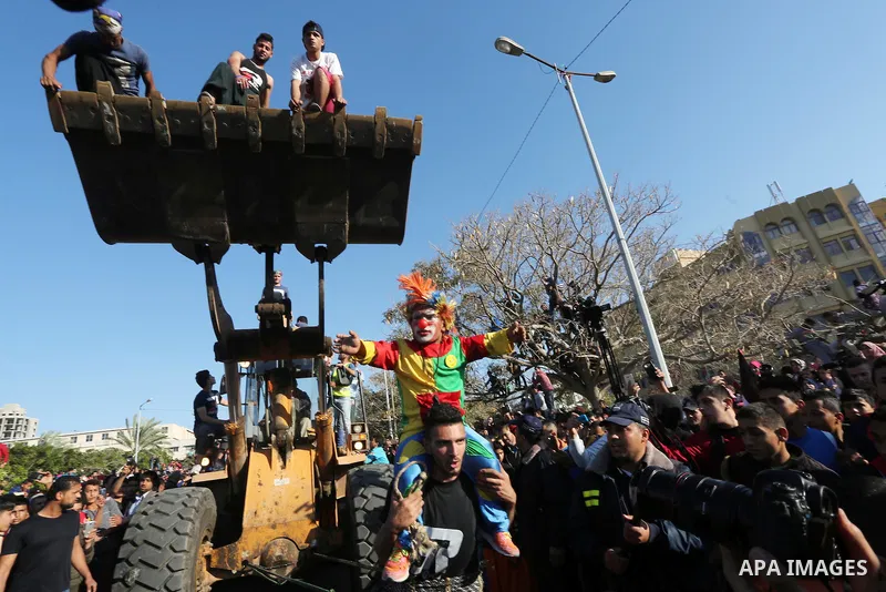 Palestinian Mohammad Baraka, nicknamed Gaza Samson, pulls a bulldozer by a rope tried around his waist as he holds a man dressed as a clown during a cultural carnival organized by Gaza Municipality in Gaza City April 1,...