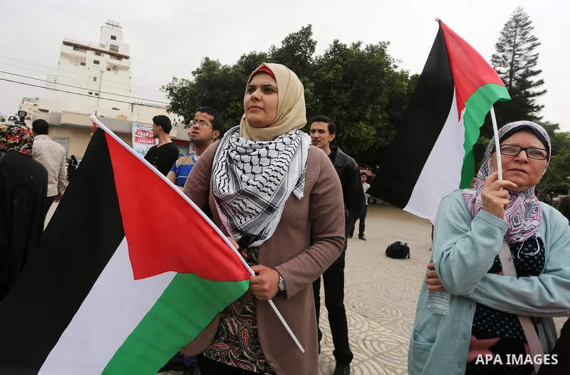 Palestinians hold national flags during a demonstration to calling for an end in the political division and the national reconciliation in Gaza city, on April 10, 2016. Photo by Mohammed Asad
