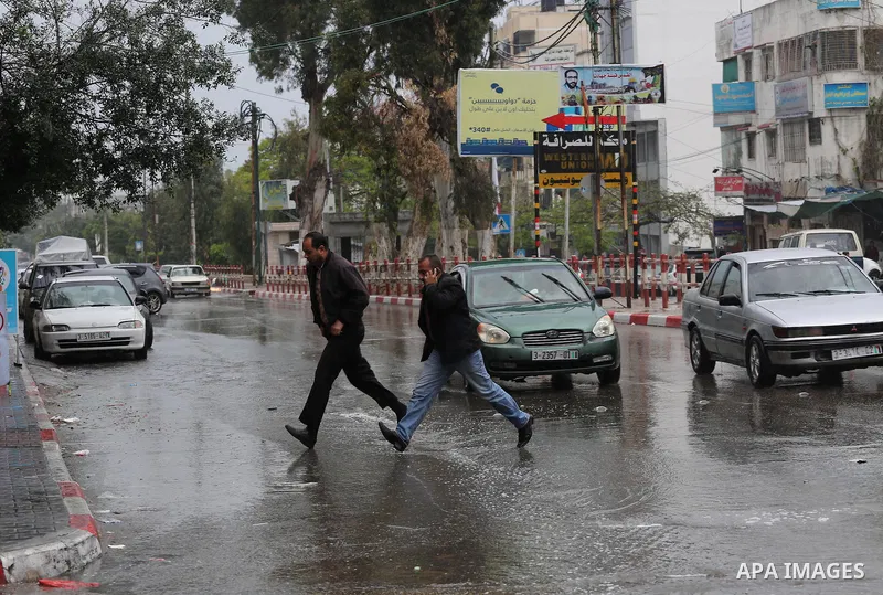 Palestinians walk in a flooded street during a rainy day, in Gaza City on April 12, 2016. Photo by Mohammed Asad