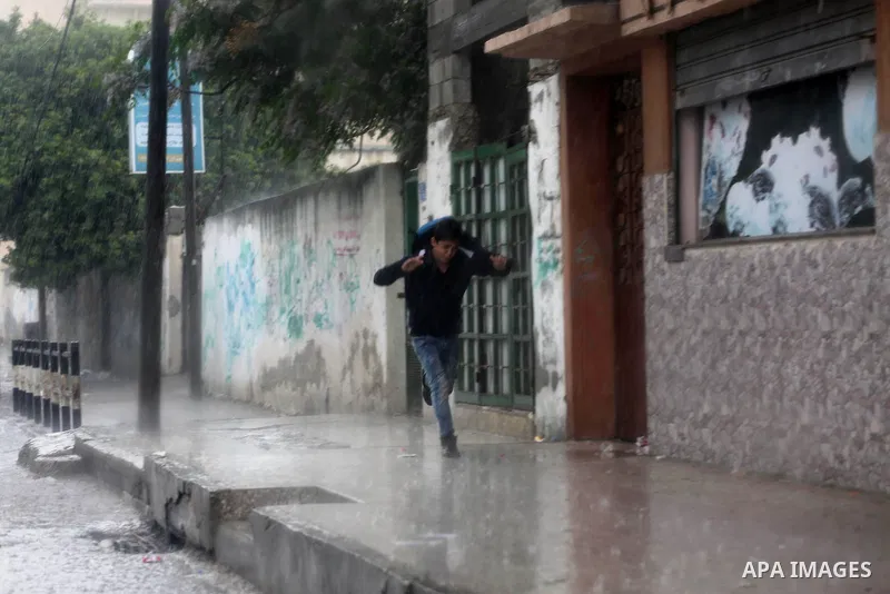 Palestinians walk in a flooded street during a rainy day, in Gaza City on April 12, 2016. Photo by Mohammed Asad