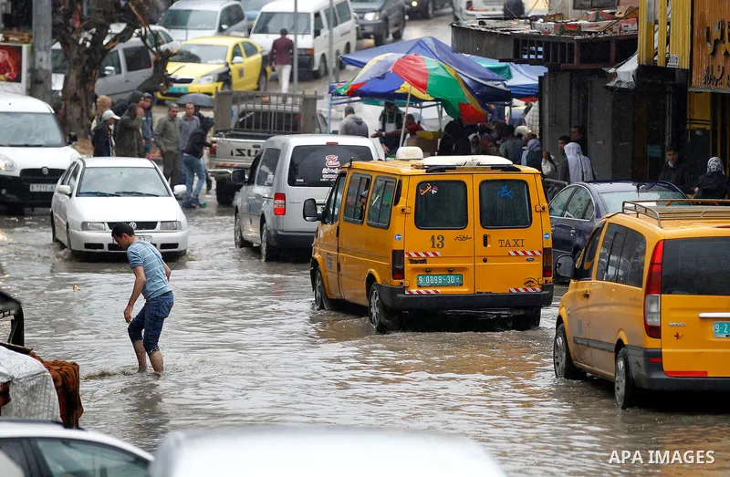 Palestinians walk in a flooded street during a rainy day, in the West Bank city of Hebron on April 12, 2016. Photo by Wisam Hashlamoun