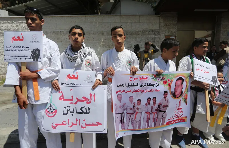 Palestinians hold banners during a protest in solidarity with the karate trainer, Hassan El-Raey against his arrest by the Israeli army, in front of Red cross office in Gaza city on April 13, 2016. Photo by Mohammed Asad