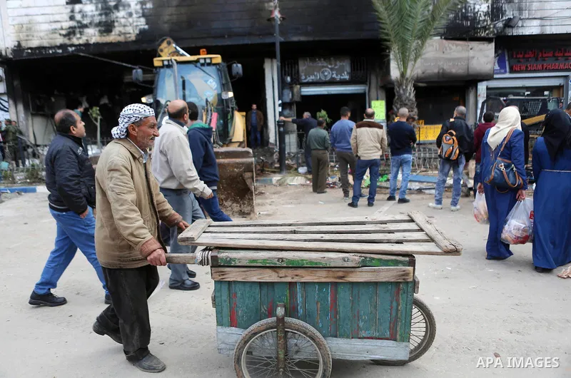 Palestinians gather around a money changer in the Palestinian political capital Ramallah after it was raided by Israeli forces, blowing up a safe and sparking a fire, on April 14, 2016. An Israeli army spokeswoman said t...