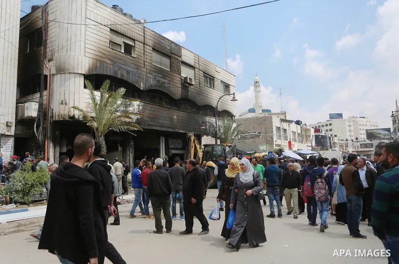 Palestinians gather around a money changer in the Palestinian political capital Ramallah after it was raided by Israeli forces, blowing up a safe and sparking a fire, on April 14, 2016. An Israeli army spokeswoman said t...