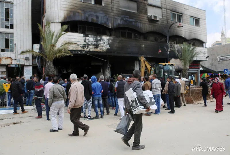 Palestinians gather around a money changer in the Palestinian political capital Ramallah after it was raided by Israeli forces, blowing up a safe and sparking a fire, on April 14, 2016. An Israeli army spokeswoman said t...