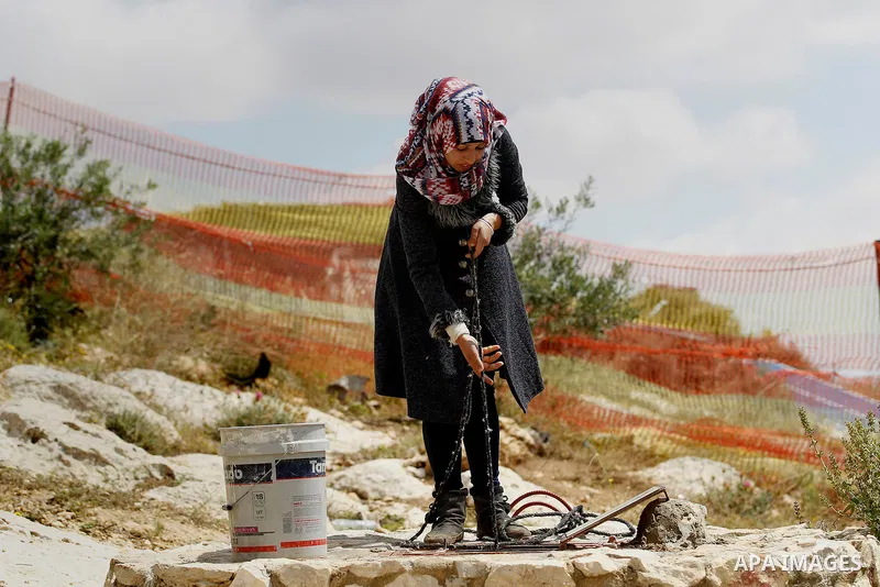 A Palestinian woman of Hawamdeh family takes water from a well outside a cave she lives in, in West Bank village of Mufagara, south of Hebron on April 14, 2016. Photo by Wisam Hashlamoun