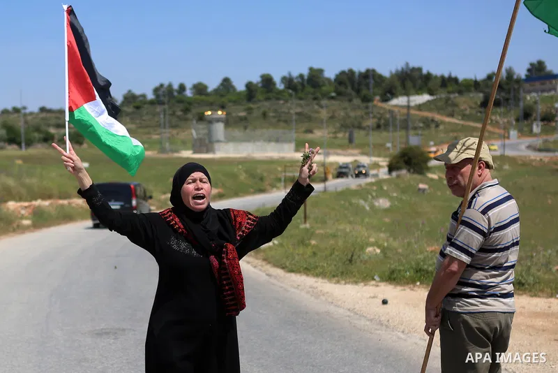 A Palestinian woman waves national flags in front of Israeli security forces during clashes following a march against Palestinian land confiscation on April 15, 2016 in the West Bank village of Nabi Saleh near Ramallah....