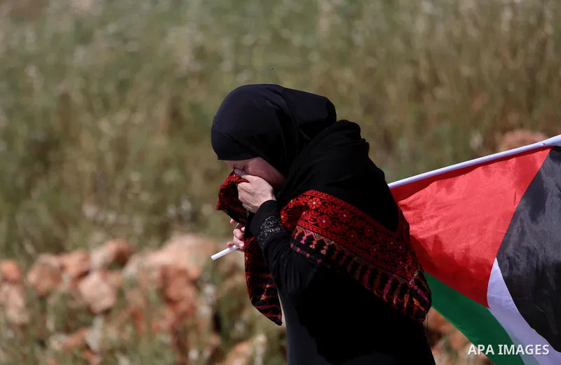 A Palestinian woman takes cover from tear gas fired by Israeli security forces during clashes following a march against Palestinian land confiscation on April 15, 2016 in the West Bank village of Nabi Saleh near Ramallah...
