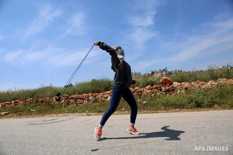 A Palestinian girl uses a slingshot to hurl stones towards Israeli security forces during clashes following a march against Palestinian land confiscation on April 15, 2016 in the West Bank village of Nabi Saleh near Rama...