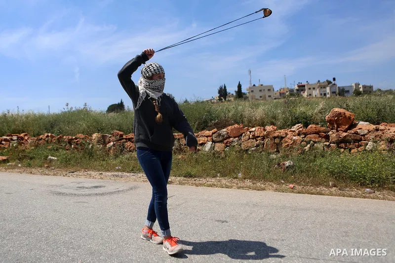 A Palestinian girl uses a slingshot to hurl stones towards Israeli security forces during clashes following a march against Palestinian land confiscation on April 15, 2016 in the West Bank village of Nabi Saleh near Rama...
