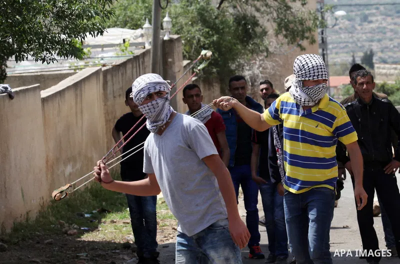 Palestinian protesters use a slingshot to hurl stones towards Israeli security forces during clashes following a weekly demonstration against the expropriation of Palestinian land by Israel in the village of Kfar Qaddum,...