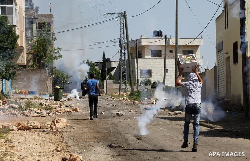 Palestinian protesters take cover from teargas fired by Israeli security forces during clashes following a weekly demonstration against the expropriation of Palestinian land by Israel in the village of Kfar Qaddum, near...