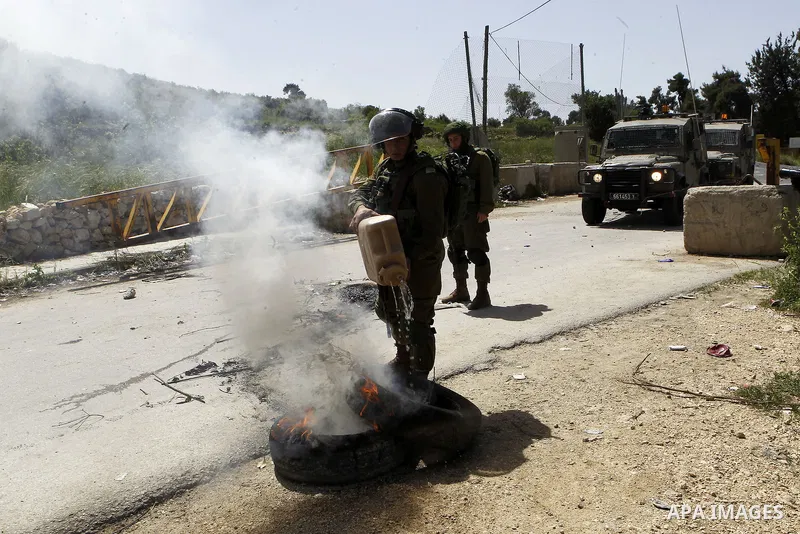 An Israeli soldier puts out a fire during clashes with Palestinian protesters in Arroub refugee camp north of the West Bank city of Hebron April 16, 2016. Photo by Wisam Hashlamoun