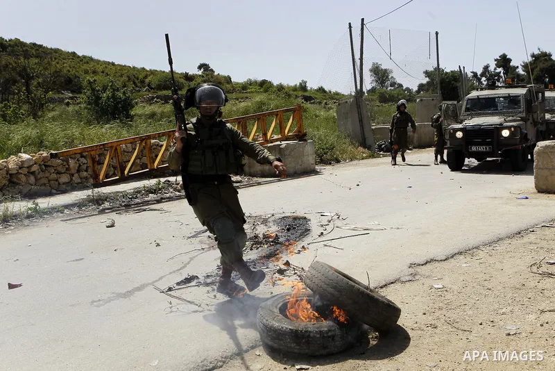 An Israeli soldier puts out a fire during clashes with Palestinian protesters in Arroub refugee camp north of the West Bank city of Hebron April 16, 2016. Photo by Wisam Hashlamoun
