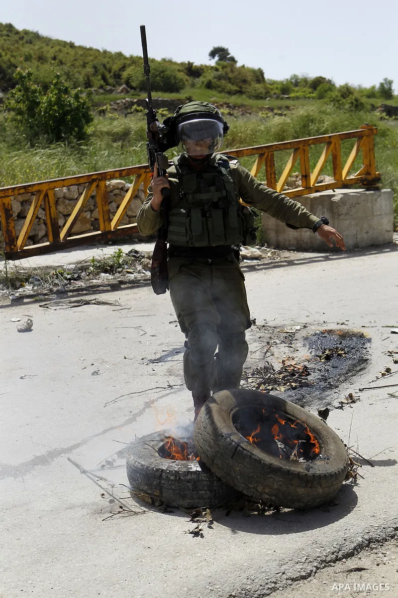 An Israeli soldier puts out a fire during clashes with Palestinian protesters in Arroub refugee camp north of the West Bank city of Hebron April 16, 2016. Photo by Wisam Hashlamoun