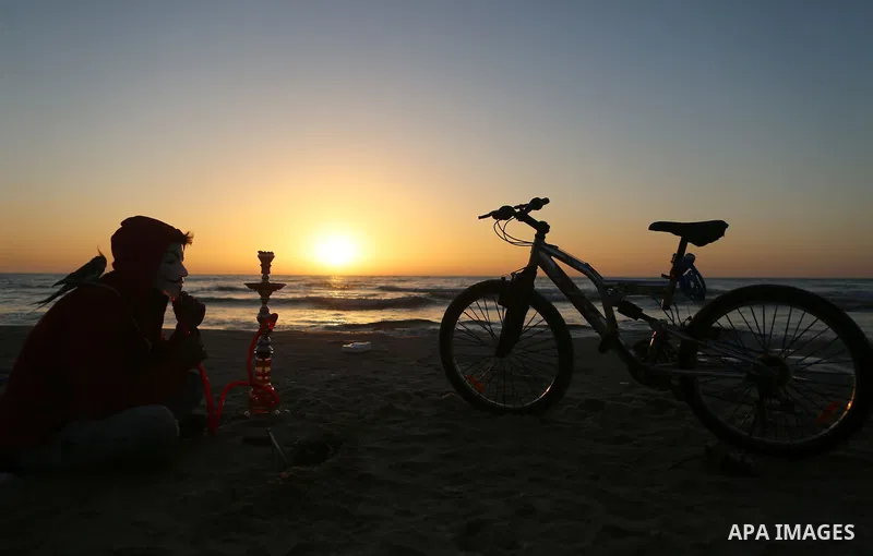 A Palestinian youth smokes flavoured tobacco water pipes or 'shisha' during sunset at the beach of the Mediterranean sea on the coast of Gaza city on April 17, 2016. Photo by Yasser Qudih