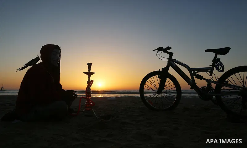 A Palestinian youth smokes flavoured tobacco water pipes or 'shisha' during sunset at the beach of the Mediterranean sea on the coast of Gaza city on April 17, 2016. Photo by Yasser Qudih