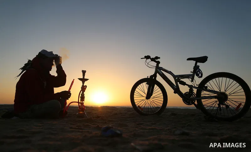 A Palestinian youth smokes flavoured tobacco water pipes or 'shisha' during sunset at the beach of the Mediterranean sea on the coast of Gaza city on April 17, 2016. Photo by Yasser Qudih