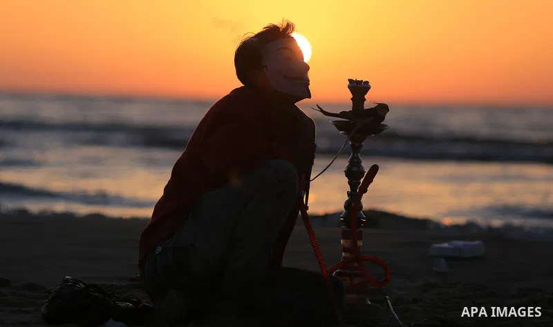 A Palestinian youth smokes flavoured tobacco water pipes or 'shisha' during sunset at the beach of the Mediterranean sea on the coast of Gaza city on April 17, 2016. Photo by Yasser Qudih