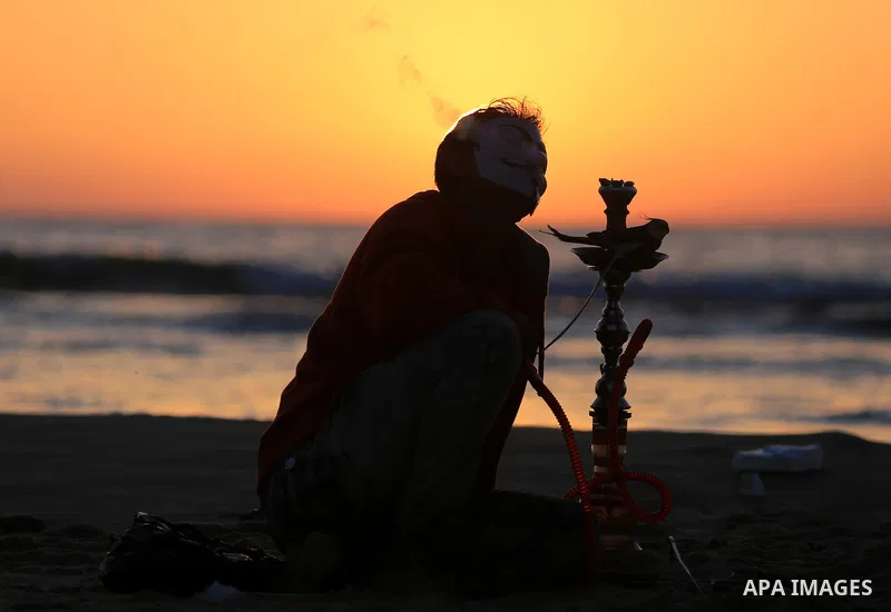 A Palestinian youth smokes flavoured tobacco water pipes or 'shisha' during sunset at the beach of the Mediterranean sea on the coast of Gaza city on April 17, 2016. Photo by Yasser Qudih