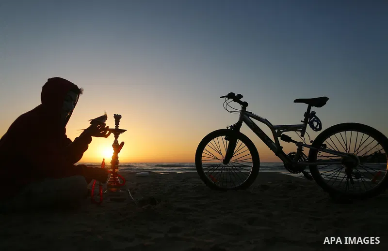 A Palestinian youth smokes flavoured tobacco water pipes or 'shisha' during sunset at the beach of the Mediterranean sea on the coast of Gaza city on April 17, 2016. Photo by Yasser Qudih