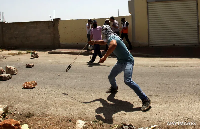 A Palestinian protester uses a slingshot to hurl stones towards Israeli security forces during clashes following a weekly demonstration against the expropriation of Palestinian land by Israel in the village of Kfar Qaddu...